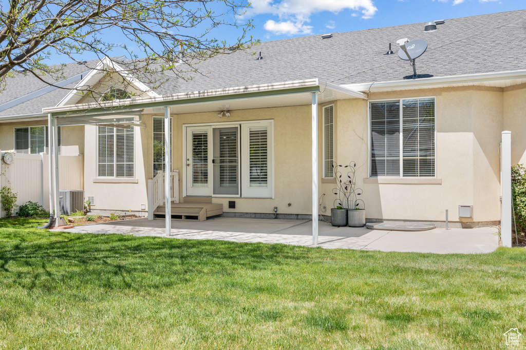 Back of house with a shingled roof, stucco siding, and a yard