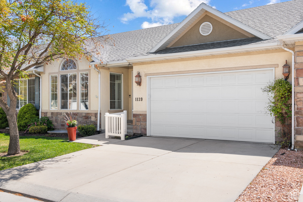 View of front of house featuring roof with shingles, stucco siding, and concrete driveway