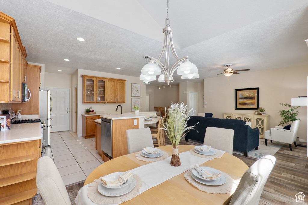 Dining area featuring a textured ceiling, light wood-type flooring, baseboards, ceiling fan with notable chandelier, and recessed lighting