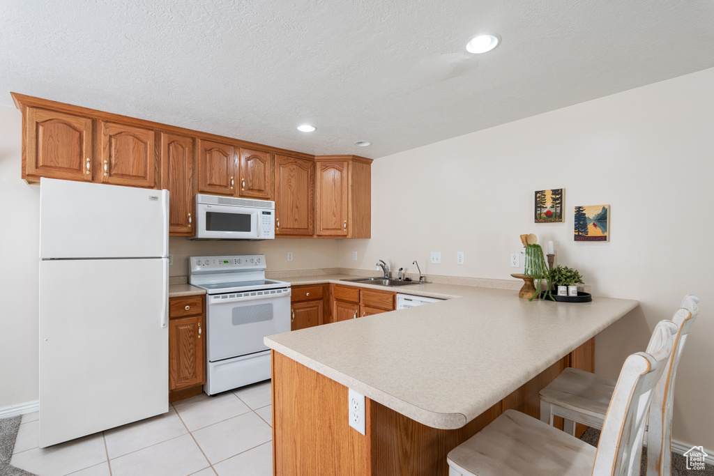 Kitchen featuring a sink, white appliances, a kitchen breakfast bar, light countertops, and a peninsula