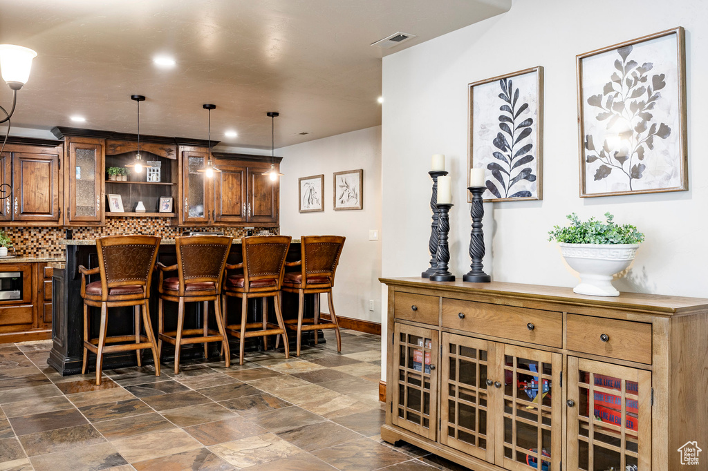 Bar featuring decorative backsplash, stone finish flooring, visible vents, and decorative light fixtures