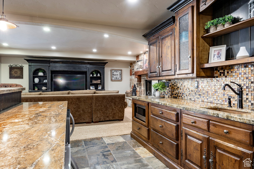 Kitchen featuring decorative backsplash, open shelves, built in microwave, a sink, and light stone counters