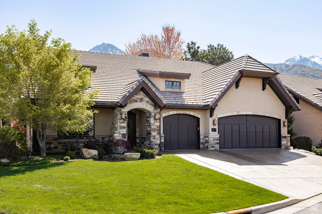 Tudor house featuring a front yard, stone siding, stucco siding, concrete driveway, and a mountain view