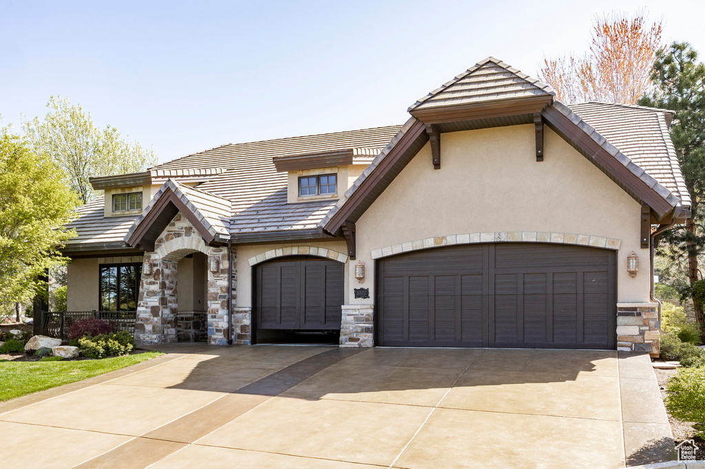 View of front facade featuring a garage, stucco siding, concrete driveway, and stone siding