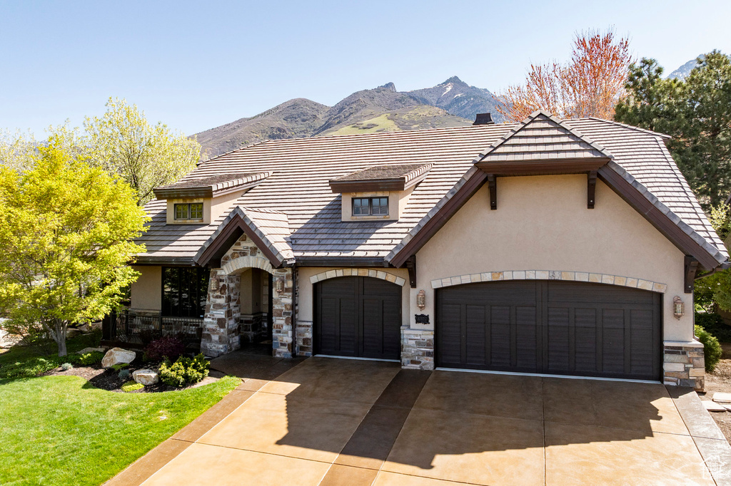 View of front of property with stone siding, a garage, stucco siding, a mountain view, and concrete driveway