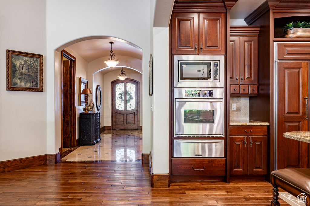 Kitchen with appliances with stainless steel finishes, arched walkways, light stone counters, a warming drawer, and hardwood / wood-style floors