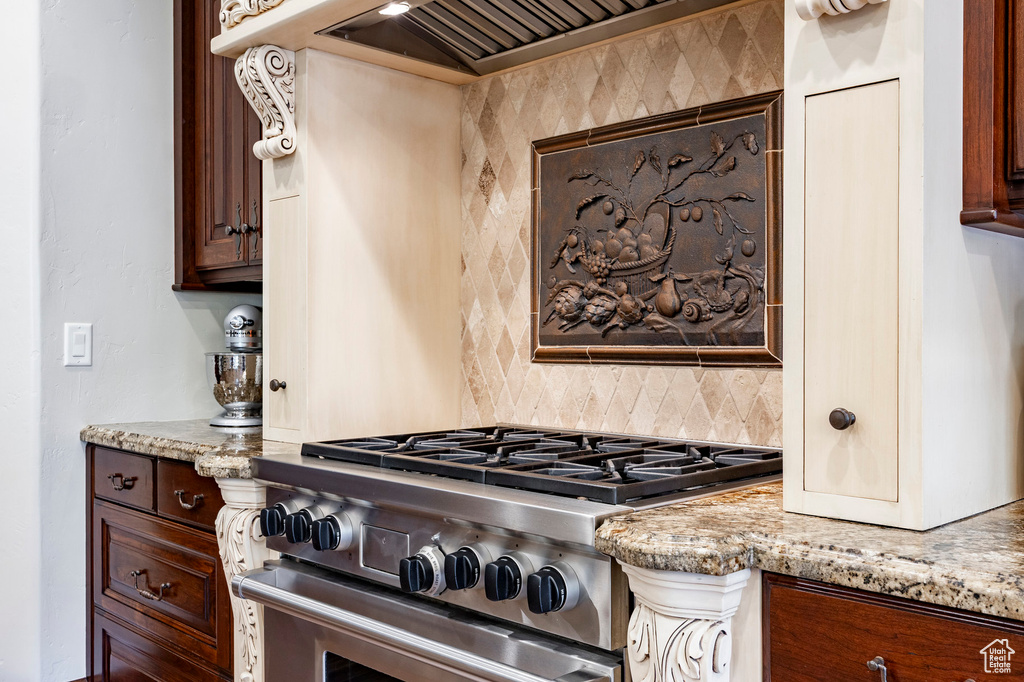 Kitchen with decorative backsplash, light stone counters, dark brown cabinets, premium range hood, and high end stove
