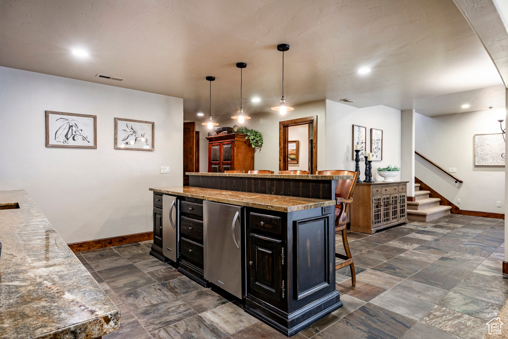 Kitchen featuring a kitchen breakfast bar, visible vents, fridge, baseboards, and dark cabinets