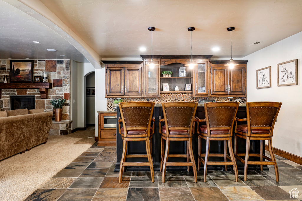 Bar with pendant lighting, arched walkways, tasteful backsplash, baseboards, and stainless steel microwave