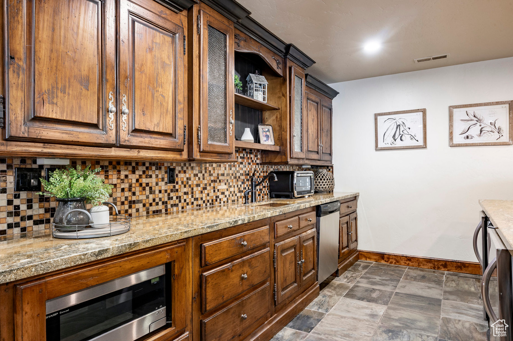 Kitchen featuring glass insert cabinets, baseboards, tasteful backsplash, light stone counters, and appliances with stainless steel finishes