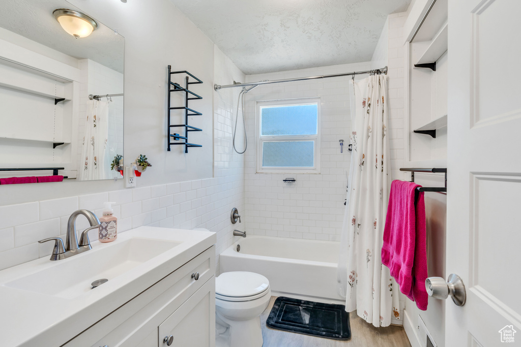 Full bath featuring vanity, shower / tub combo with curtain, toilet, a textured ceiling, and tile walls