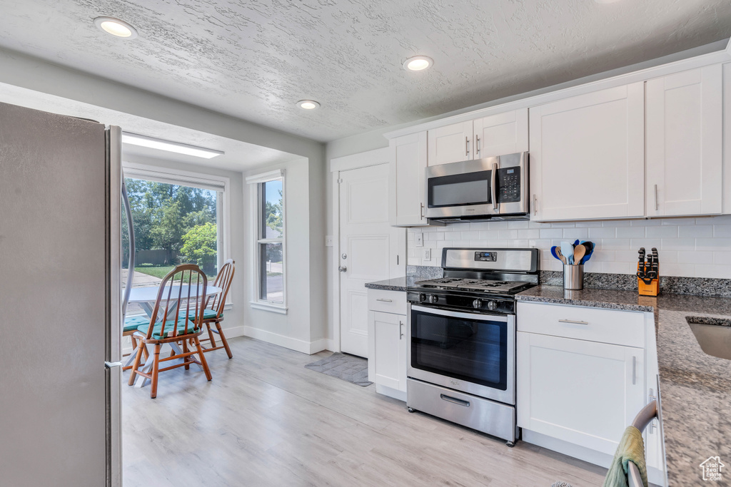 Kitchen with decorative backsplash, baseboards, white cabinetry, dark stone countertops, and appliances with stainless steel finishes