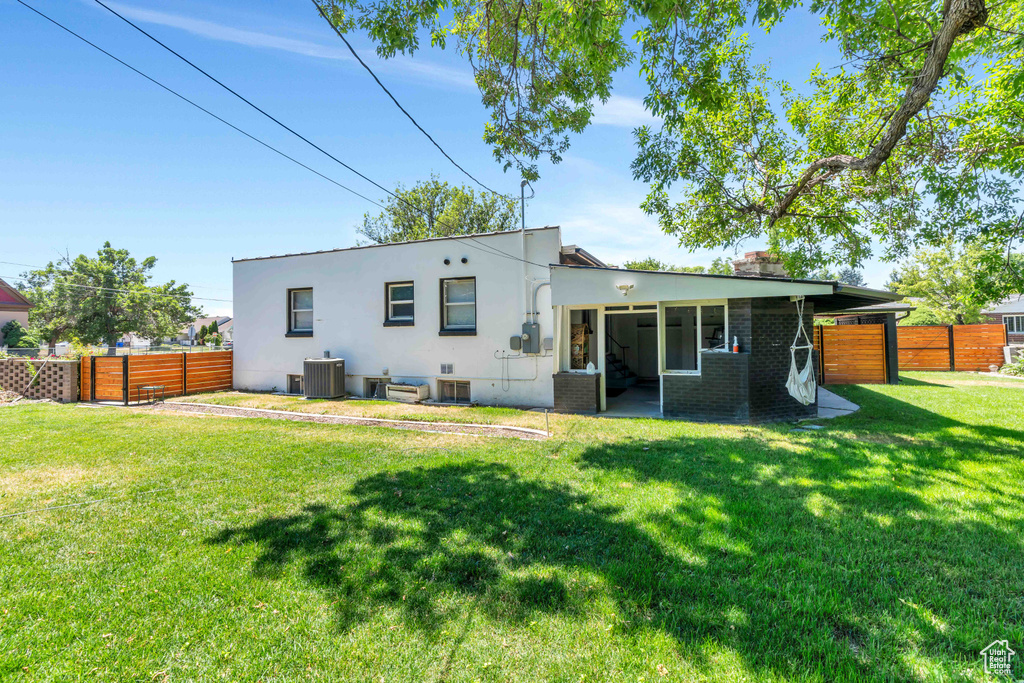 Back of house featuring a lawn, stucco siding, fence, and central air condition unit