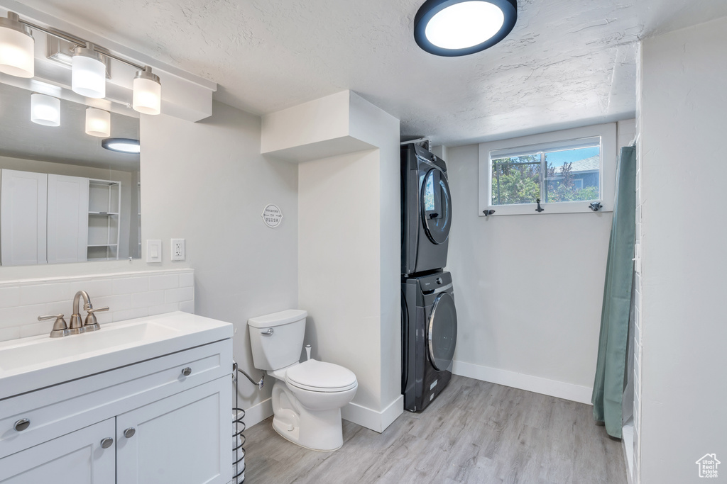 Full bath with vanity, stacked washer and dryer, wood finished floors, toilet, and backsplash