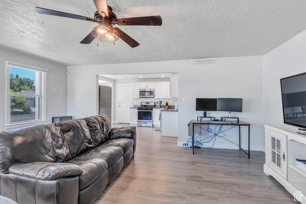 Living area featuring ceiling fan, a textured ceiling, visible vents, and light wood-style flooring