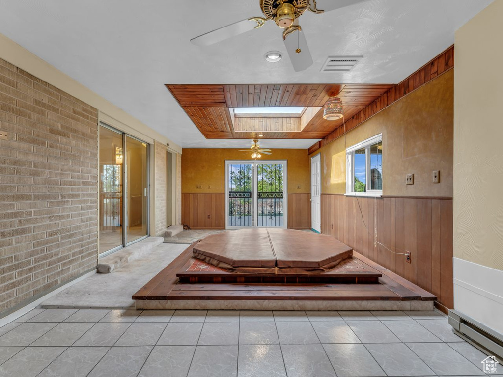 Interior space featuring a ceiling fan, wood walls, visible vents, and baseboard heating