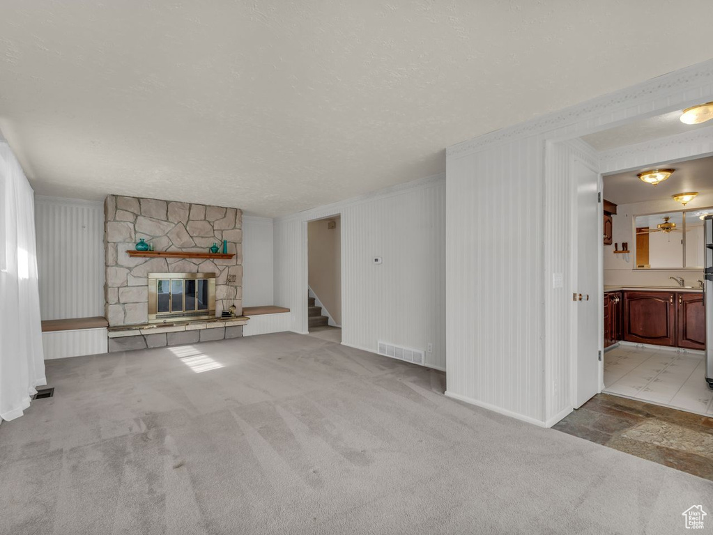 Unfurnished living room featuring a textured ceiling, a stone fireplace, visible vents, carpet, and stairs