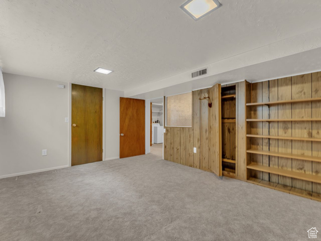 Finished below grade area featuring visible vents, a textured ceiling, carpet floors, and wooden walls