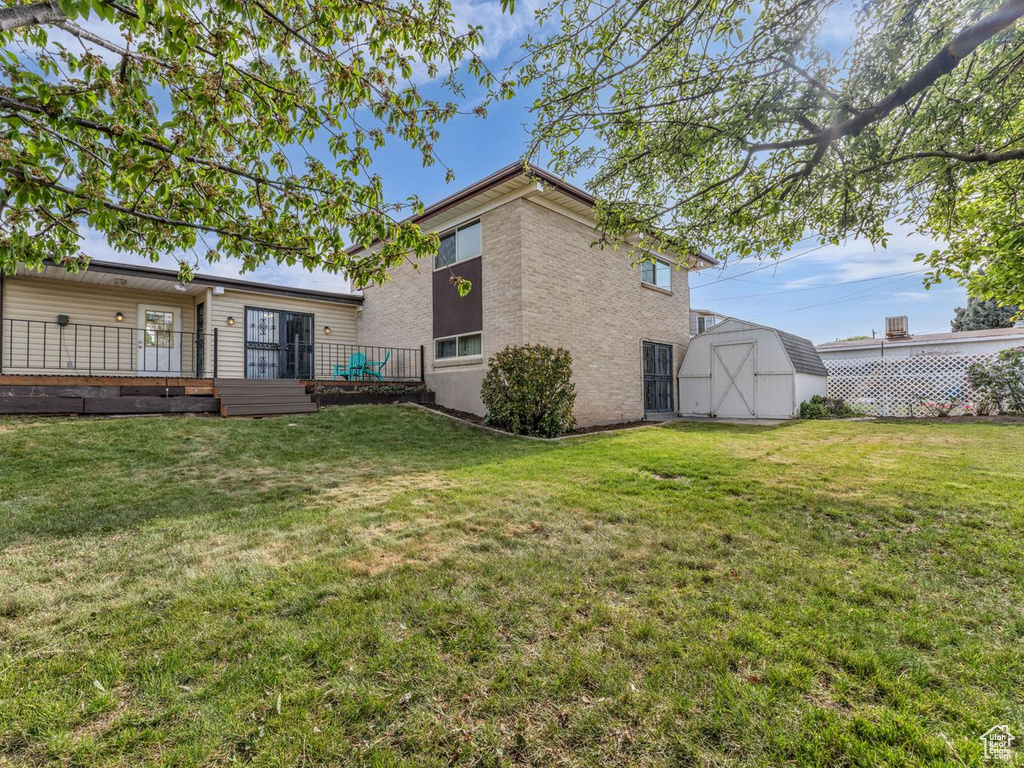 Back of property featuring a storage shed, brick siding, a yard, and an outdoor structure