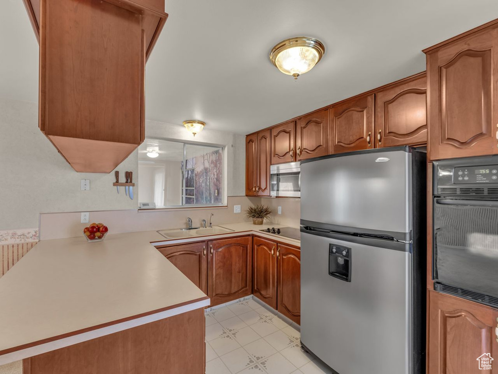 Kitchen featuring brown cabinets, a sink, light countertops, a peninsula, and black appliances