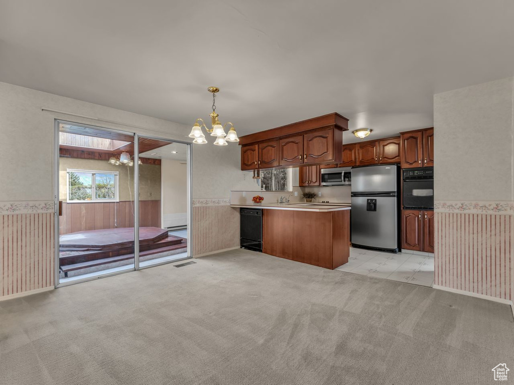 Kitchen featuring decorative light fixtures, a wainscoted wall, black appliances, an inviting chandelier, and light carpet