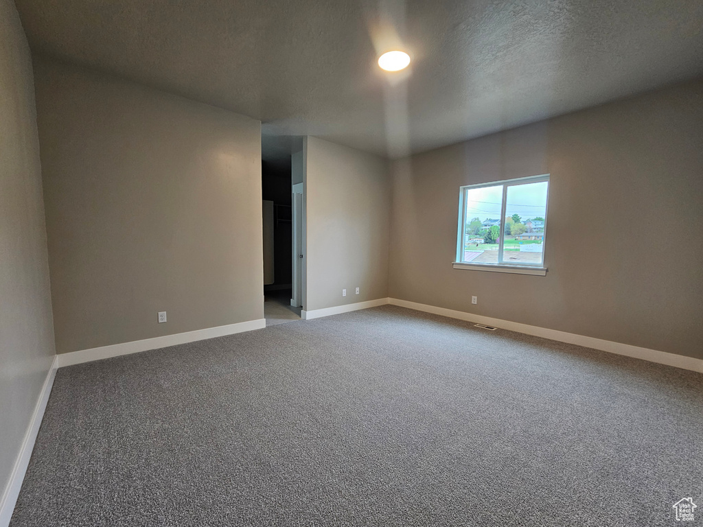 Carpeted spare room with baseboards, a textured ceiling, and visible vents