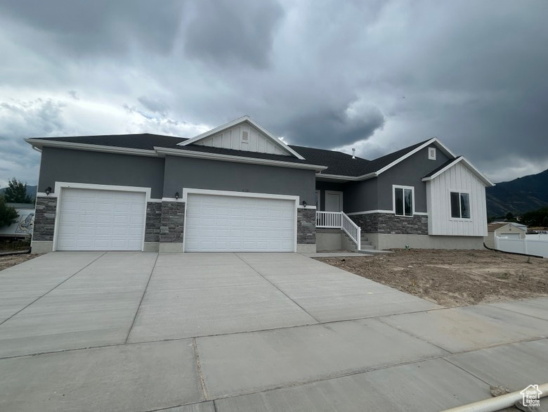 View of front of house featuring stone siding, a garage, concrete driveway, and stucco siding