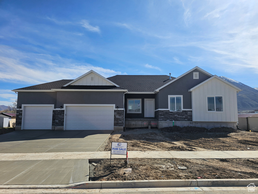 View of front of home with an attached garage, stone siding, board and batten siding, stucco siding, and driveway