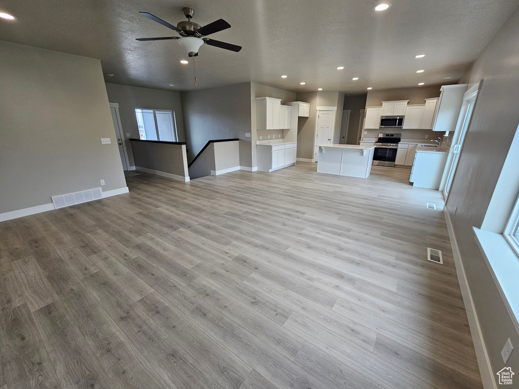 Unfurnished living room featuring a ceiling fan, visible vents, light wood-style flooring, and recessed lighting