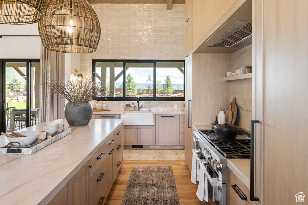 Kitchen featuring high end stainless steel range, light wood-style floors, light stone counters, a sink, and a wealth of natural light