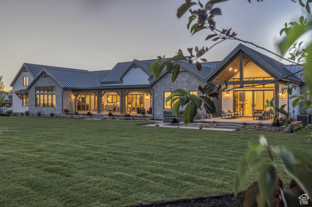 Rear view of house with a lawn, a standing seam roof, metal roof, and stone siding