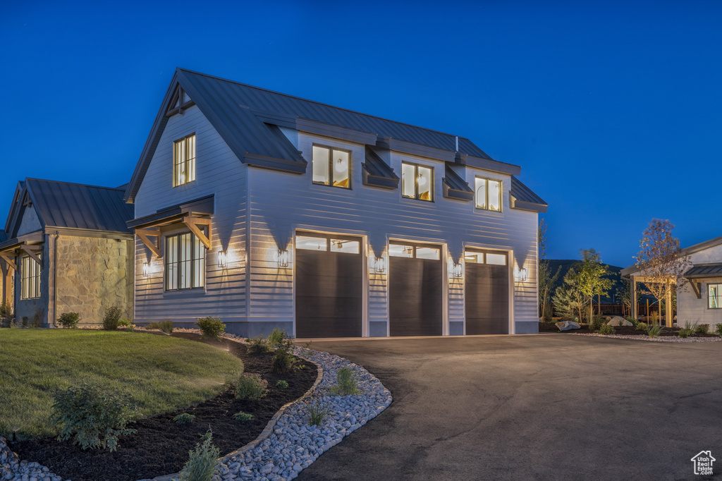 View of front of house with a standing seam roof, driveway, metal roof, a garage, and a yard
