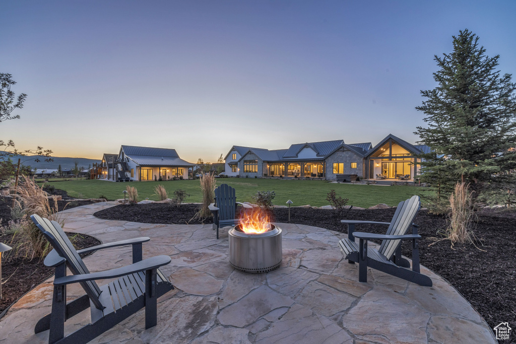 Patio terrace at dusk featuring a lawn and a fire pit