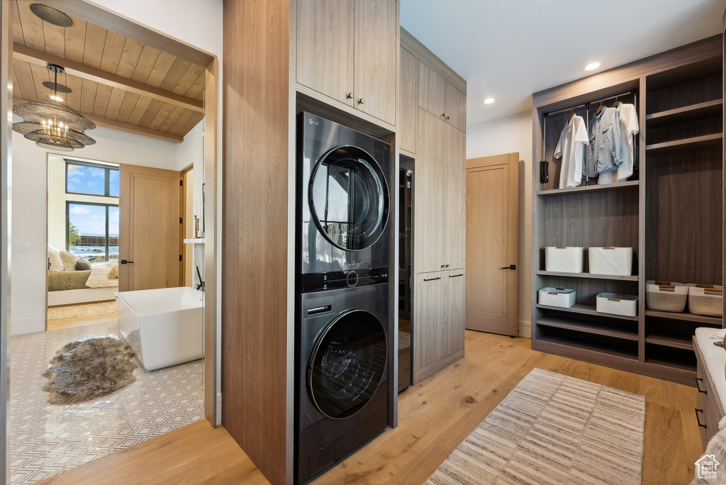 Laundry room with light wood-style floors, stacked washing maching and dryer, and wooden ceiling