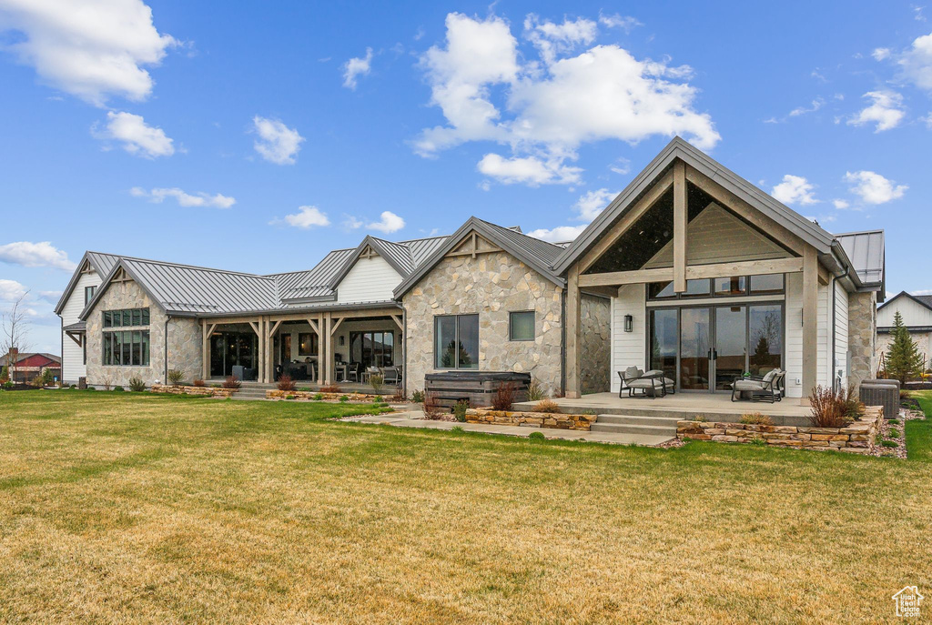 Back of house with a hot tub, a patio area, a standing seam roof, a lawn, and metal roof