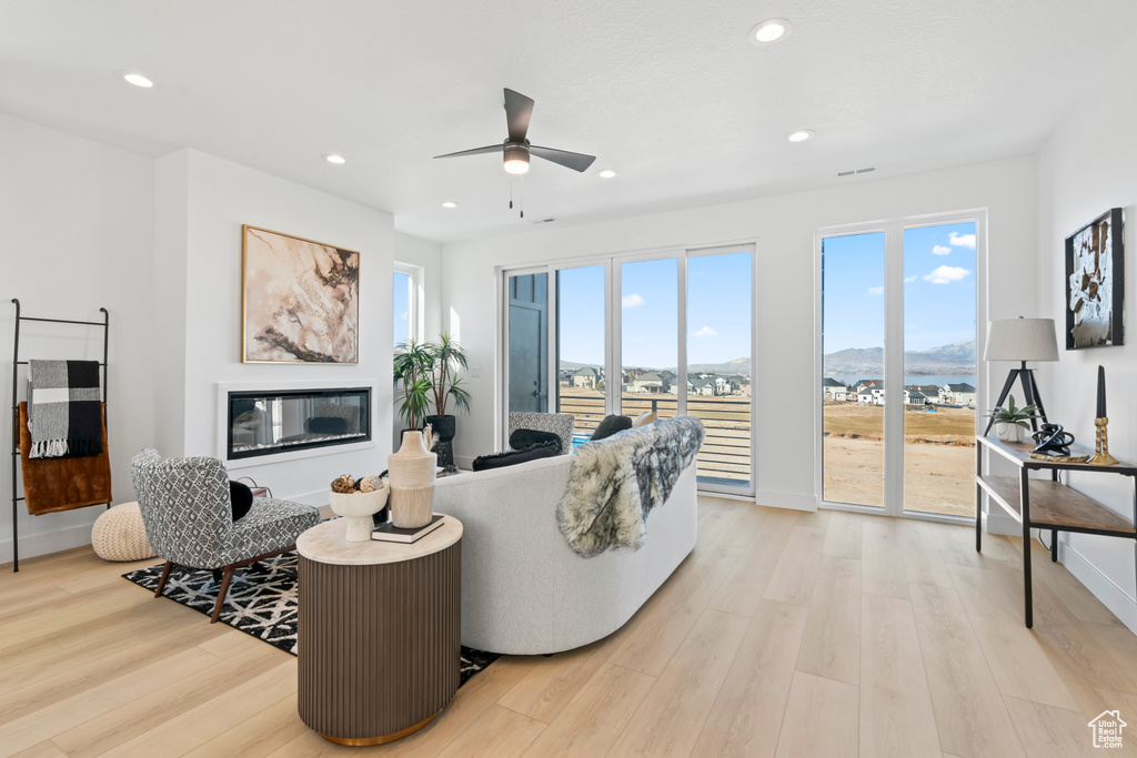 Living area with recessed lighting, a ceiling fan, light wood finished floors, and a glass covered fireplace