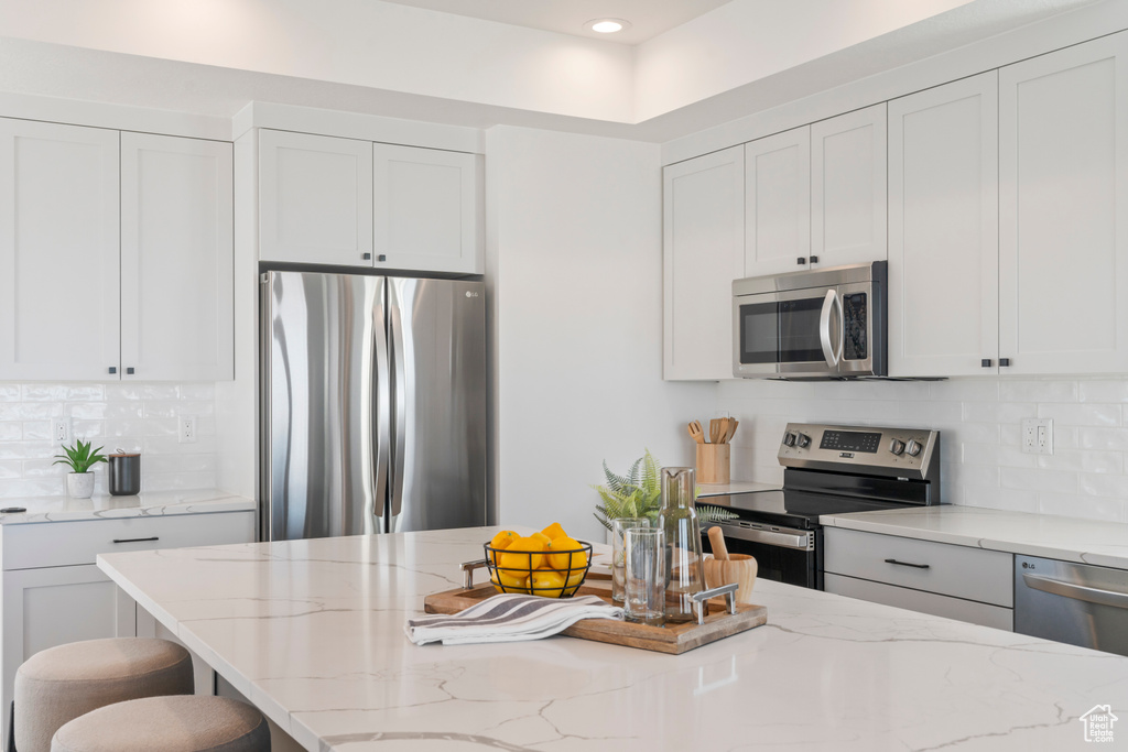 Kitchen with white cabinets, tasteful backsplash, light stone countertops, and stainless steel appliances