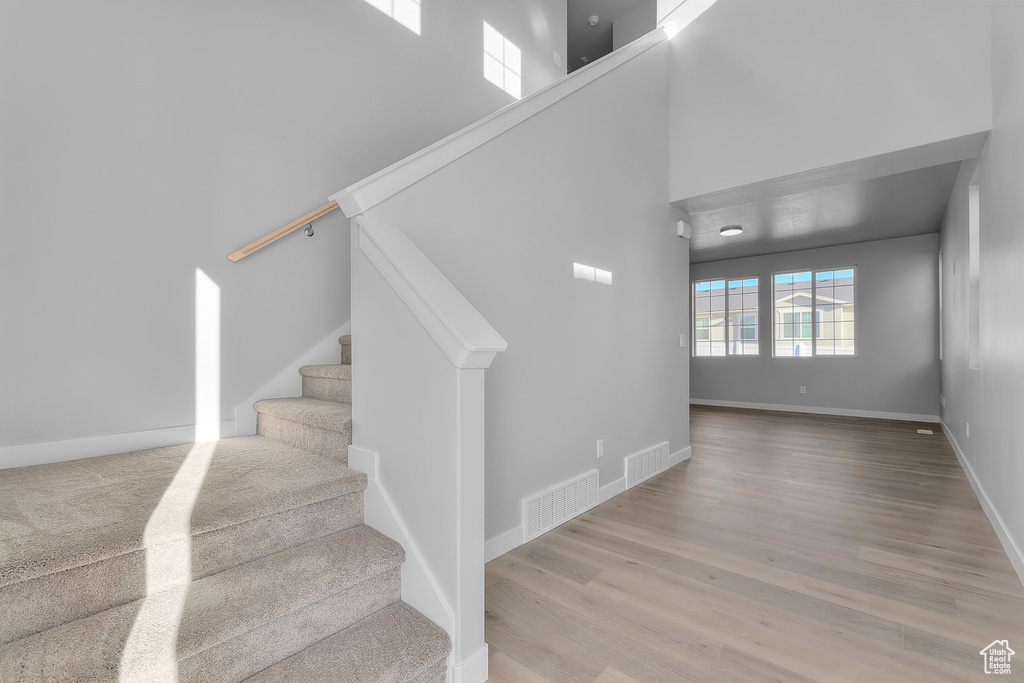 Stairs with baseboards, a high ceiling, visible vents, and wood finished floors
