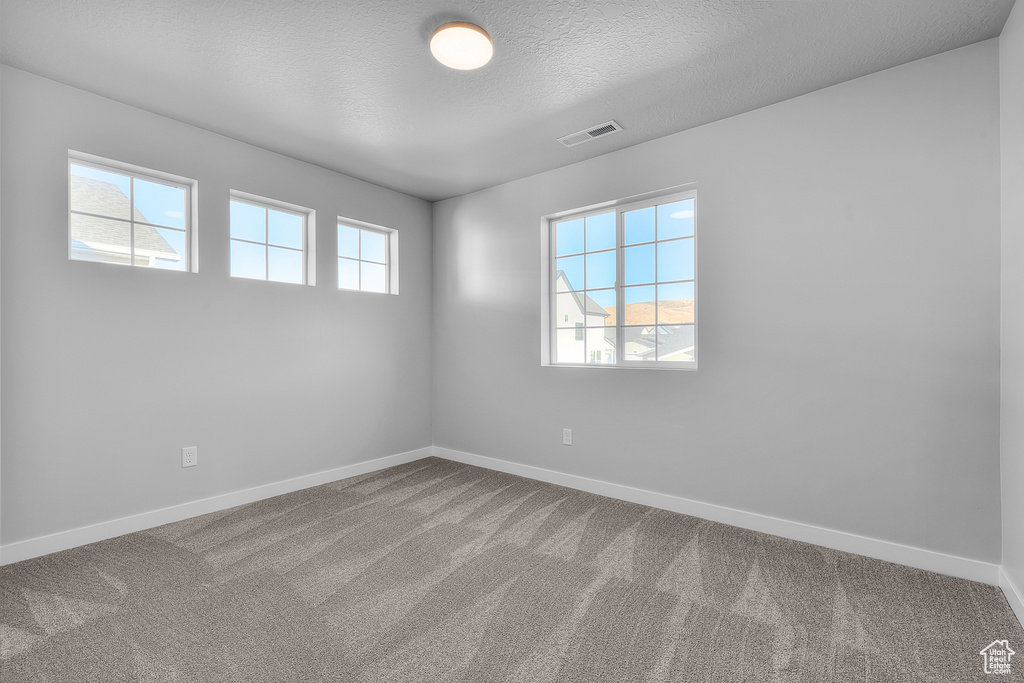 Carpeted spare room featuring visible vents, a textured ceiling, and baseboards