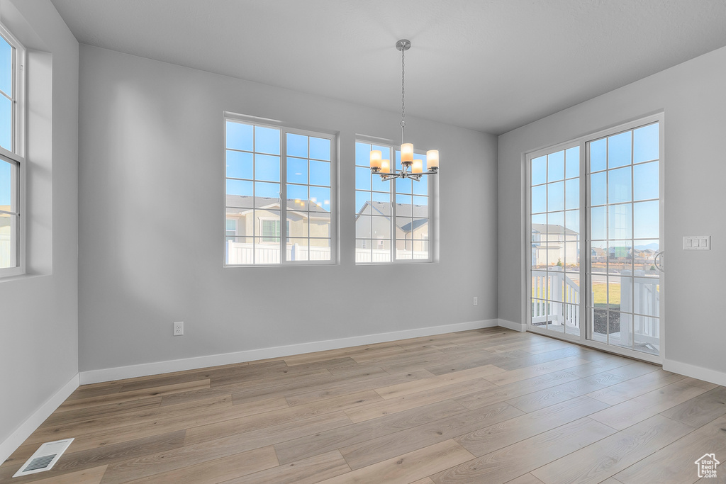 Empty room featuring a notable chandelier, visible vents, baseboards, and light wood finished floors