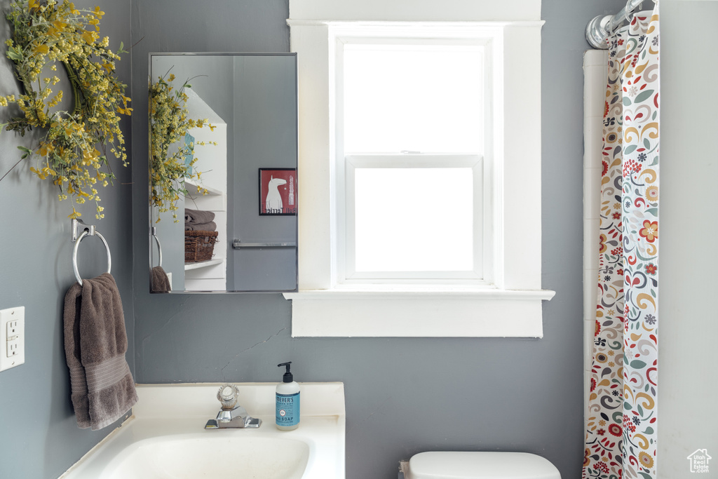 Bathroom featuring a sink, a shower with curtain, toilet, and a wealth of natural light
