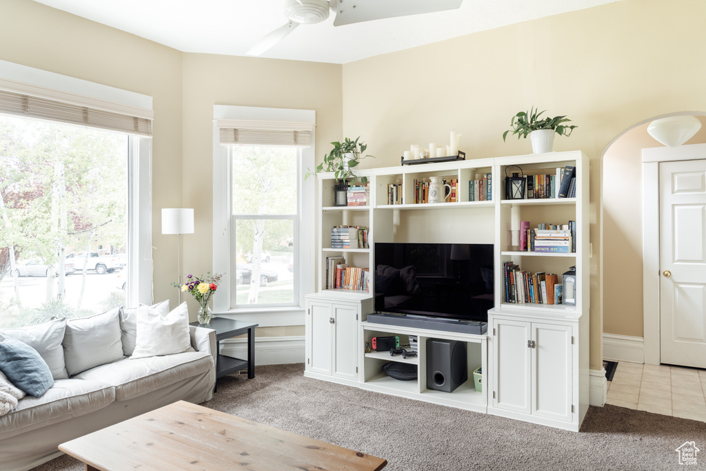 Carpeted living room with arched walkways and ceiling fan