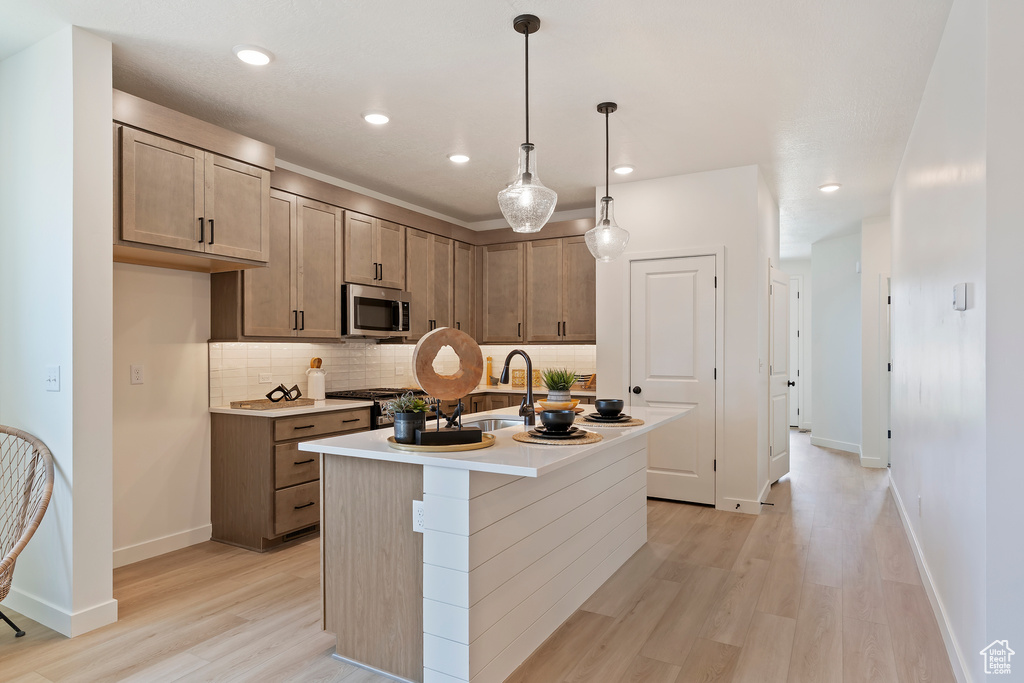 Kitchen with stainless steel microwave, light wood-style floors, backsplash, recessed lighting, and hanging light fixtures