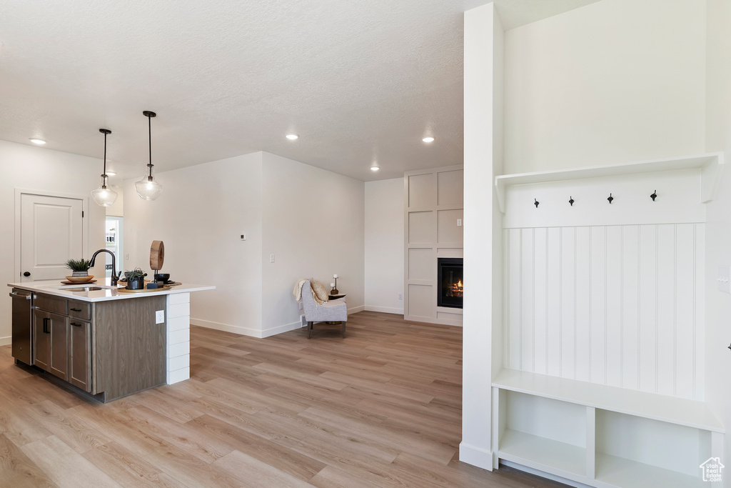 Kitchen featuring light wood-type flooring, recessed lighting, light countertops, a center island with sink, and a tiled fireplace