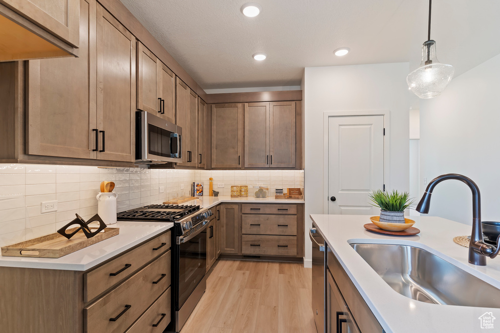 Kitchen with appliances with stainless steel finishes, light wood-type flooring, hanging light fixtures, light countertops, and decorative backsplash