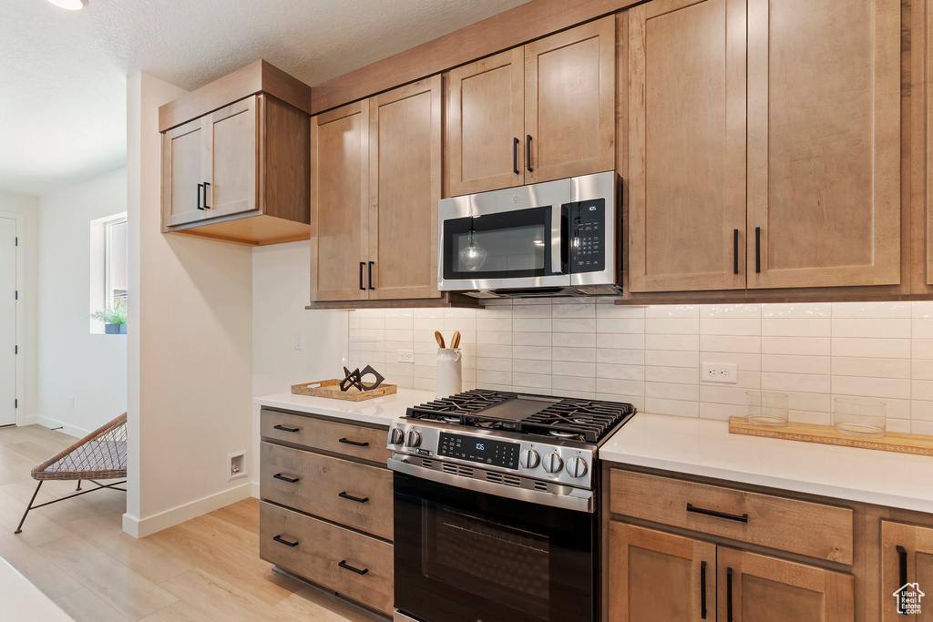 Kitchen with appliances with stainless steel finishes, light wood-style flooring, light countertops, and decorative backsplash