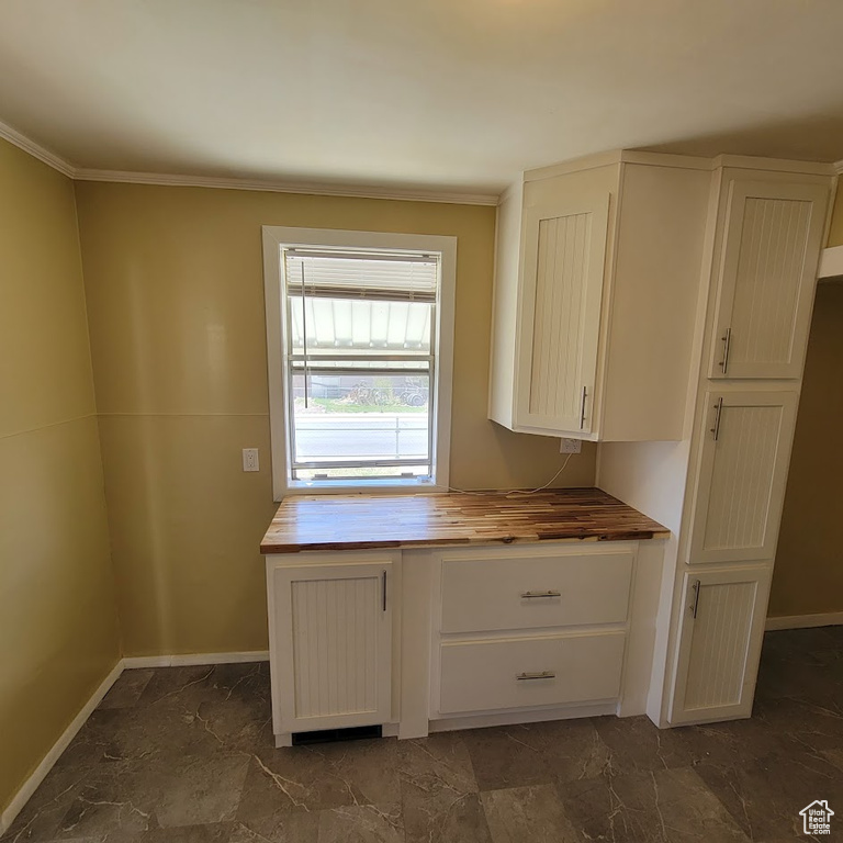 Kitchen featuring baseboards, crown molding, white cabinets, and wooden counters