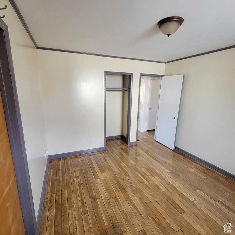 Unfurnished bedroom featuring baseboards, ornamental molding, multiple closets, and wood finished floors