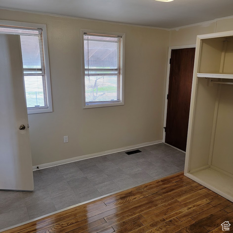 Unfurnished bedroom featuring baseboards, wood finished floors, visible vents, ornamental molding, and a closet