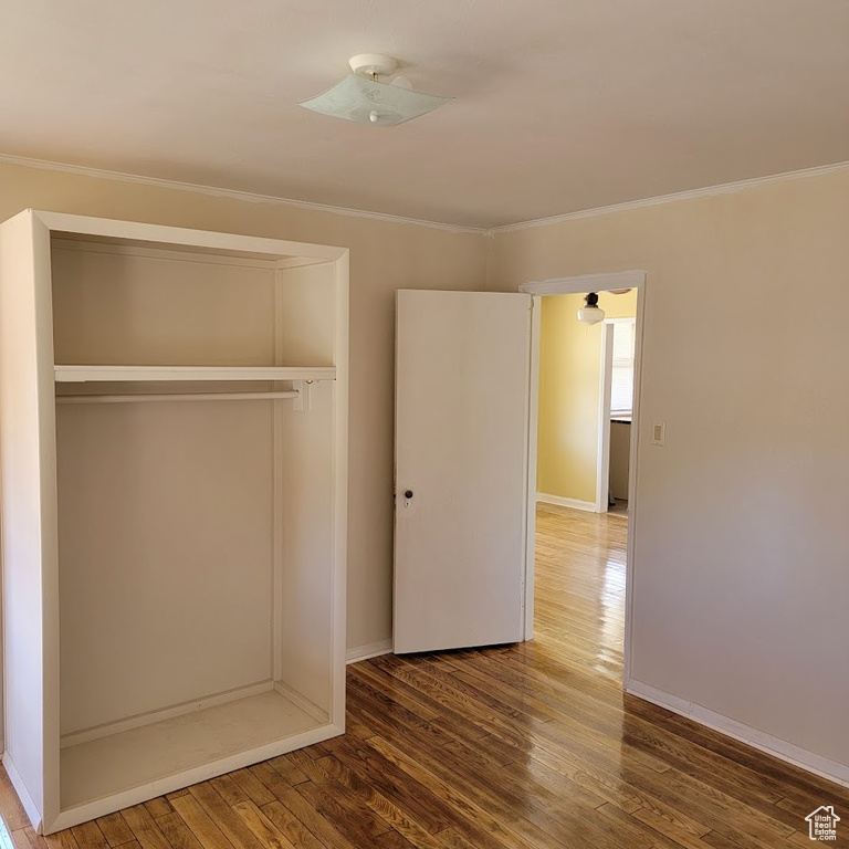 Unfurnished bedroom featuring crown molding, baseboards, a closet, and wood finished floors